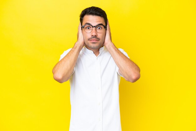 Hombre guapo joven sobre fondo amarillo aislado frustrado y cubriendo las orejas