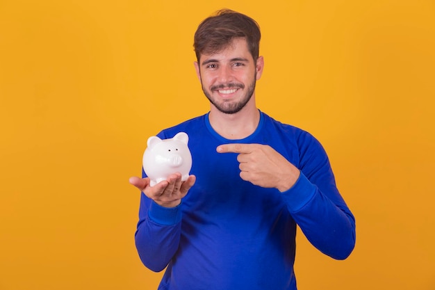 Hombre guapo joven sobre fondo amarillo aislado sosteniendo una gran alcancía