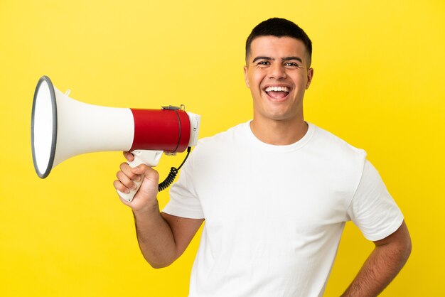 Hombre guapo joven sobre fondo amarillo aislado sosteniendo un megáfono y sonriendo