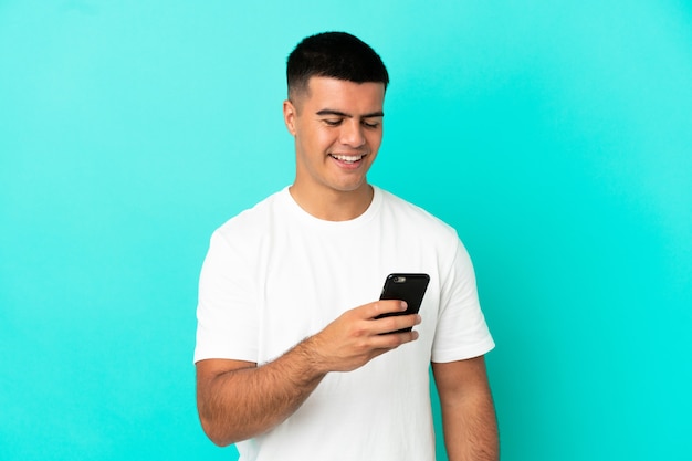 Hombre guapo joven sobre fondo azul aislado enviando un mensaje o correo electrónico con el móvil