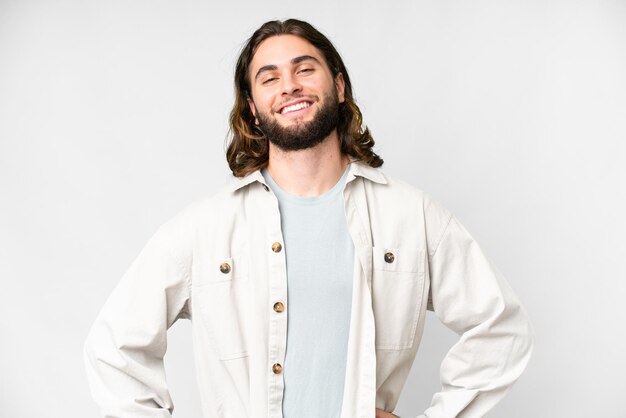 Hombre guapo joven sobre fondo blanco aislado posando con los brazos en la cadera y sonriendo