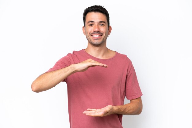 Hombre guapo joven sobre fondo blanco aislado sosteniendo copyspace imaginario en la palma para insertar un anuncio