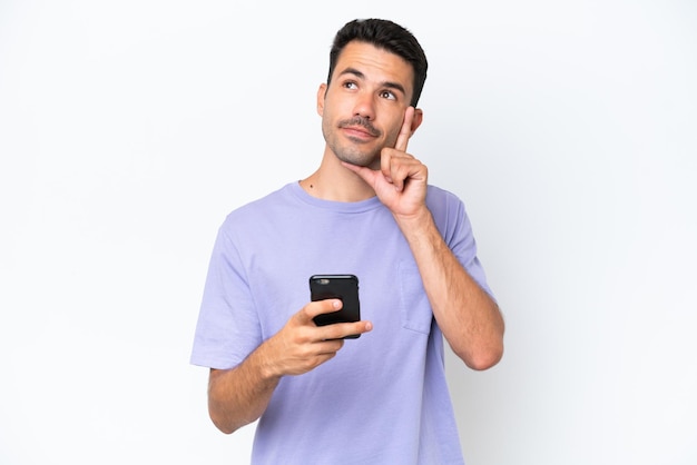 Hombre guapo joven sobre fondo blanco aislado usando teléfono móvil y pensando