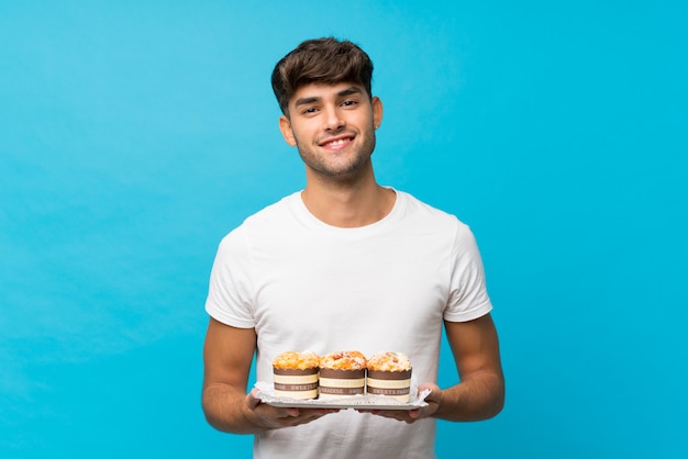 Hombre guapo joven sobre pared azul aislada con mini tortas