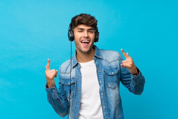 Hombre guapo joven sobre pared azul aislada usando el móvil con auriculares y baile