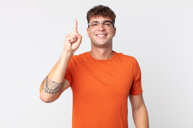 Hombre guapo joven sonriendo alegre y felizmente, apuntando hacia arriba con una mano para copiar el espacio