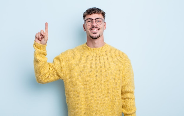 Hombre guapo joven sonriendo alegre y felizmente, apuntando hacia arriba con una mano para copiar el espacio