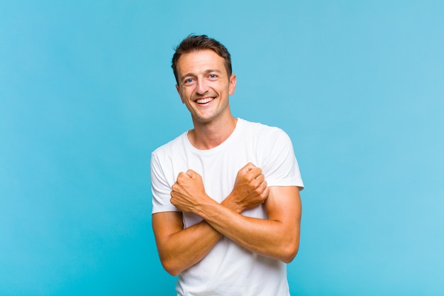 Hombre guapo joven sonriendo alegremente y celebrando, con los puños apretados y los brazos cruzados, sintiéndose feliz y positivo