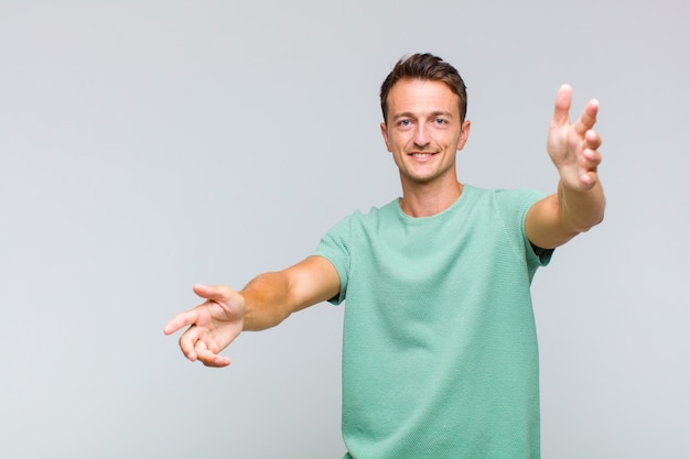 Hombre guapo joven sonriendo alegremente dando un abrazo de bienvenida cálido, amistoso y amoroso, sintiéndose feliz y adorable