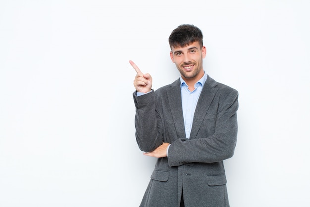 Hombre guapo joven sonriendo alegremente y mirando hacia los lados, preguntándose, pensando o teniendo una idea contra la pared blanca