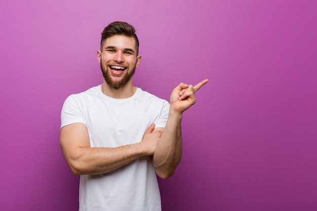 Hombre guapo joven sonriendo alegremente señalando con el dedo lejos