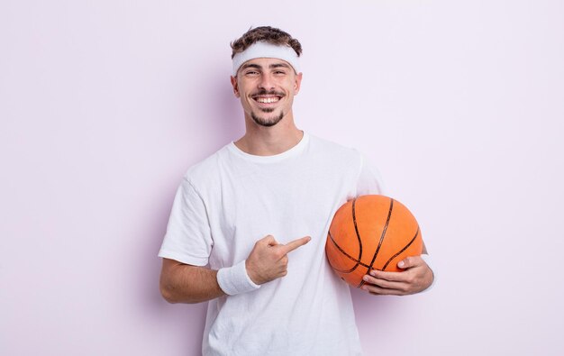 Hombre guapo joven sonriendo alegremente, sintiéndose feliz y apuntando hacia un lado. concepto de baloncesto