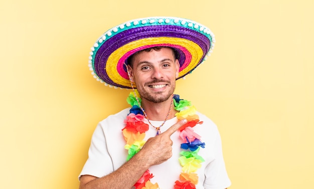 Hombre guapo joven sonriendo alegremente, sintiéndose feliz y apuntando hacia un lado. concepto de fiesta mexicana