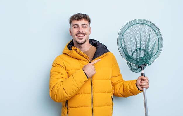 Hombre guapo joven sonriendo alegremente, sintiéndose feliz y apuntando hacia un lado. concepto de pescador