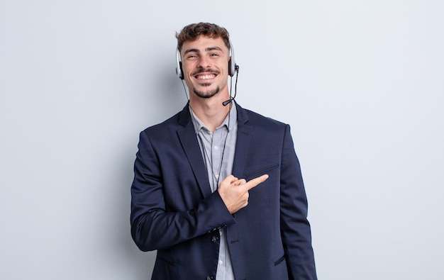 Hombre guapo joven sonriendo alegremente, sintiéndose feliz y apuntando hacia un lado. concepto de telemarketer