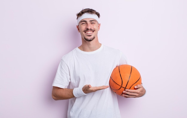 Hombre guapo joven sonriendo alegremente, sintiéndose feliz y mostrando un concepto. concepto de baloncesto