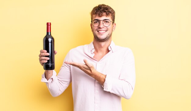 Hombre guapo joven sonriendo alegremente, sintiéndose feliz y mostrando un concepto. concepto de botella de vino
