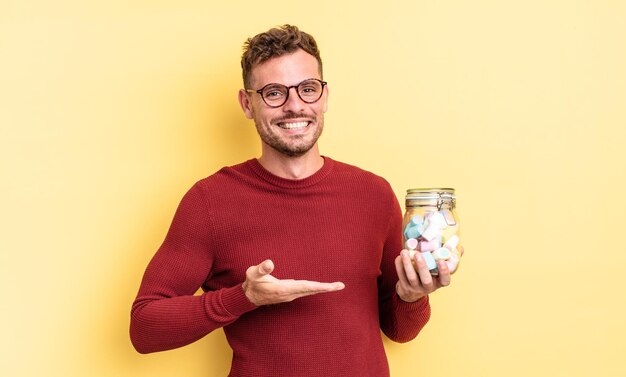 Hombre guapo joven sonriendo alegremente, sintiéndose feliz y mostrando un concepto. concepto de caramelos de gelatina