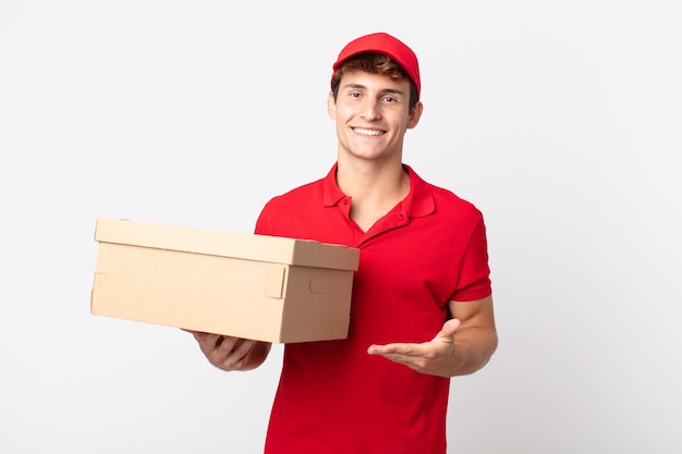 Hombre guapo joven sonriendo alegremente, sintiéndose feliz y mostrando un concepto de servicio de paquete de entrega de concepto.