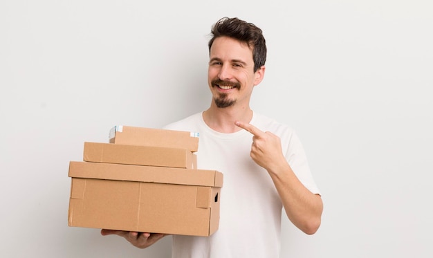 Hombre guapo joven sonriendo alegremente sintiéndose feliz y señalando el concepto de cajas de envío lateral