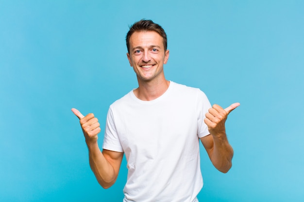 Hombre guapo joven sonriendo con alegría y luciendo feliz, sintiéndose despreocupado y positivo con ambos pulgares hacia arriba