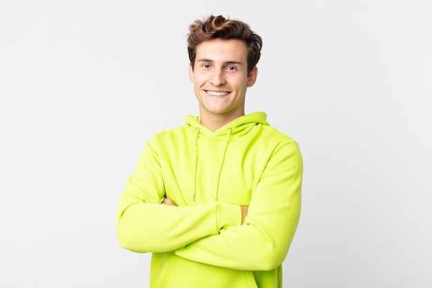 Hombre guapo joven sonriendo a la cámara con los brazos cruzados y una expresión feliz, confiada y satisfecha, vista lateral