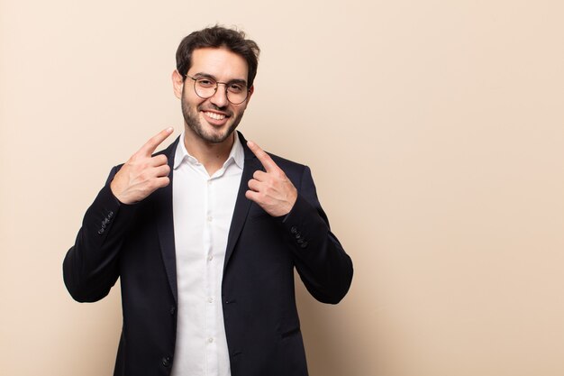 Hombre guapo joven sonriendo con confianza apuntando a su propia sonrisa amplia, actitud positiva, relajada y satisfecha