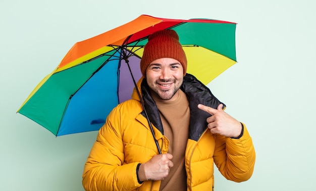 Hombre guapo joven sonriendo con confianza apuntando a su propio concepto de lluvia y paraguas de sonrisa amplia