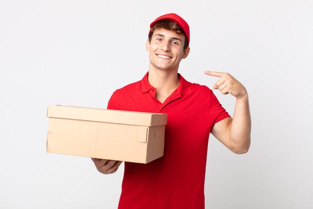 Hombre guapo joven sonriendo con confianza apuntando a su propio concepto de servicio de paquete de entrega de amplia sonrisa.
