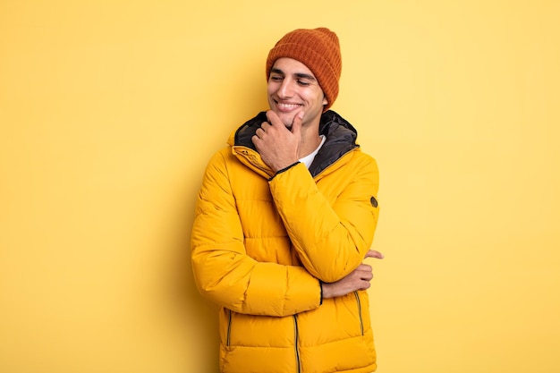 Hombre guapo joven sonriendo con una expresión feliz y segura con la mano en la barbilla. concepto de invierno