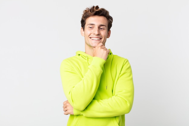 Hombre guapo joven sonriendo con una expresión feliz y segura con la mano en la barbilla, preguntándose y mirando hacia un lado