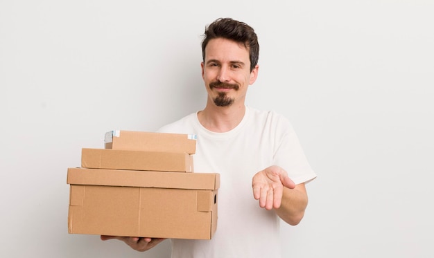 Hombre guapo joven sonriendo felizmente con amabilidad y ofreciendo y mostrando un concepto de concepto de cajas de envío