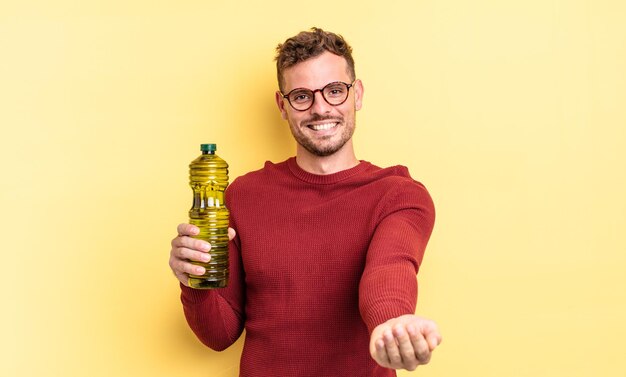 Hombre guapo joven sonriendo felizmente con amable y ofreciendo y mostrando un concepto. concepto de aceite de oliva