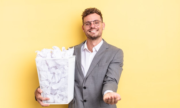 Hombre guapo joven sonriendo felizmente con amable y ofreciendo y mostrando un concepto de concepto de basura de bolas de papel