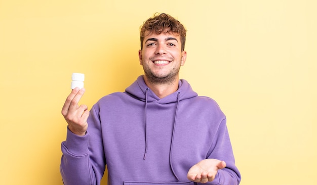 Hombre guapo joven sonriendo felizmente con amable y ofreciendo y mostrando un concepto. concepto de botella de pastillas