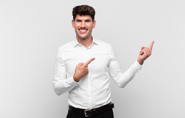 Hombre guapo joven sonriendo felizmente y apuntando hacia un lado y hacia arriba con ambas manos mostrando el objeto en el espacio de la copia