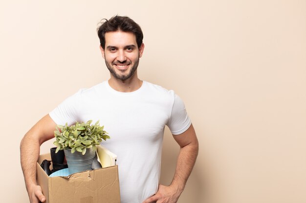 Hombre guapo joven sonriendo felizmente con una mano en la cadera y actitud confiada, positiva, orgullosa y amistosa