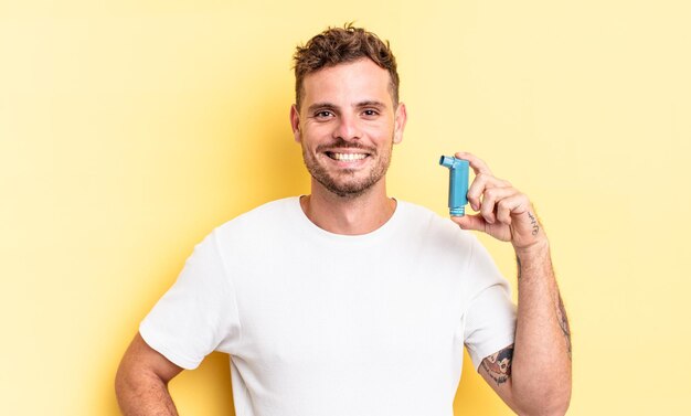 Hombre guapo joven sonriendo felizmente con una mano en la cadera y un concepto de asma confiado