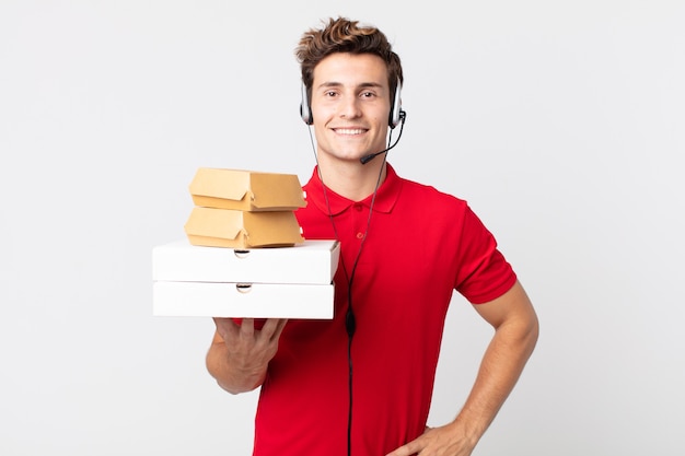 Hombre guapo joven sonriendo felizmente con una mano en la cadera y confiado. llevar concepto de comida rápida