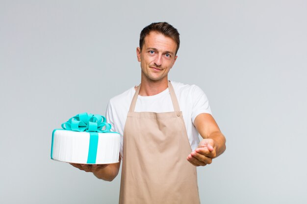 Hombre guapo joven sonriendo felizmente con mirada amistosa, segura y positiva, ofreciendo y mostrando un objeto o concepto