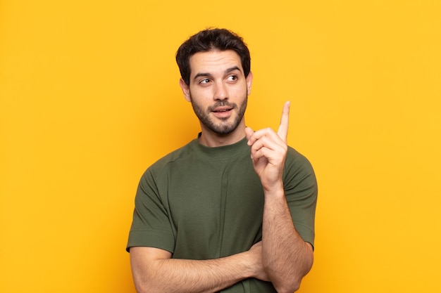 Hombre guapo joven sonriendo felizmente y mirando hacia los lados, preguntándose, pensando o teniendo una idea