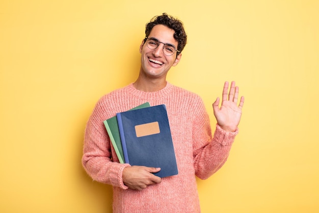 Hombre guapo joven sonriendo felizmente, saludando con la mano, dándote la bienvenida y saludándote. concepto de cuaderno