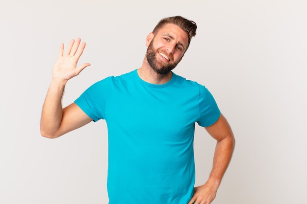 Hombre guapo joven sonriendo felizmente, saludando con la mano, dándote la bienvenida y saludándote. concepto de fitness