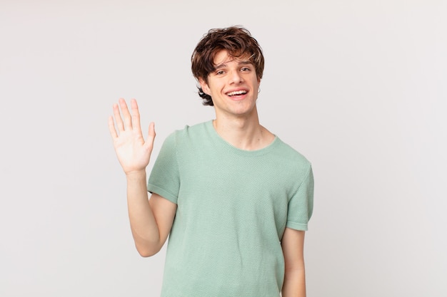 Hombre guapo joven sonriendo felizmente, saludando con la mano, dándote la bienvenida y saludándote