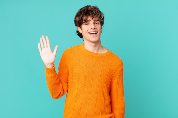 Hombre guapo joven sonriendo felizmente, saludando con la mano, dándote la bienvenida y saludándote