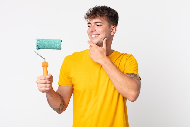 Hombre guapo joven sonriendo felizmente y soñando despierto o dudando. concepto de casa de pintura