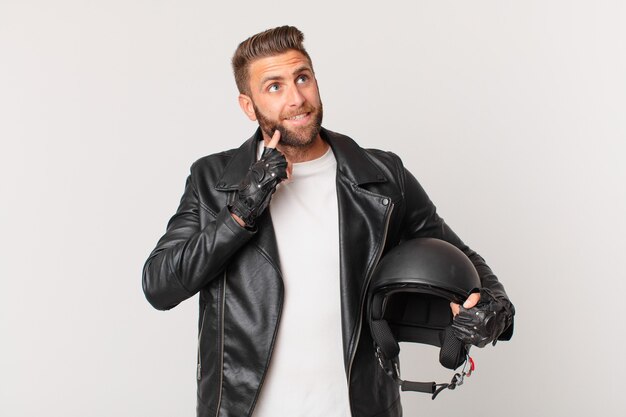 Hombre guapo joven sonriendo felizmente y soñando despierto o dudando. concepto de casco de moto