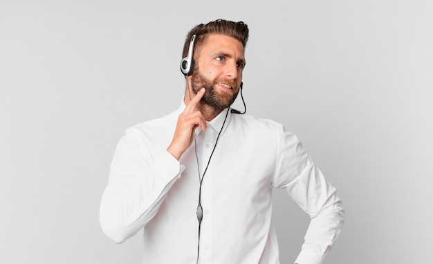 Hombre guapo joven sonriendo felizmente y soñando despierto o dudando. concepto de telemarketing