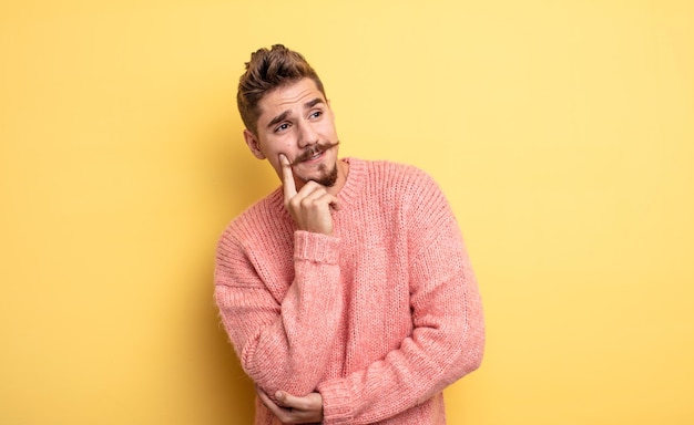 Hombre guapo joven sonriendo felizmente y soñando despierto o dudando mirando hacia el lado extraño concepto de bigote