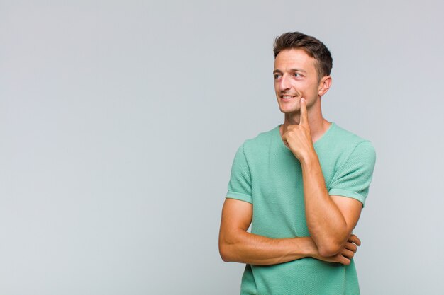 Hombre guapo joven sonriendo felizmente y soñando despierto o dudando, mirando hacia un lado